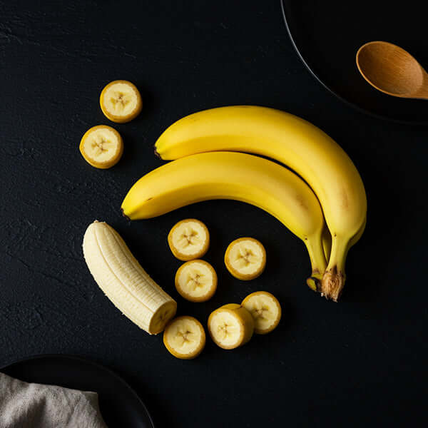 Fresh bananas and sliced banana pieces arranged on a dark surface, showcasing the vibrant yellow banana.