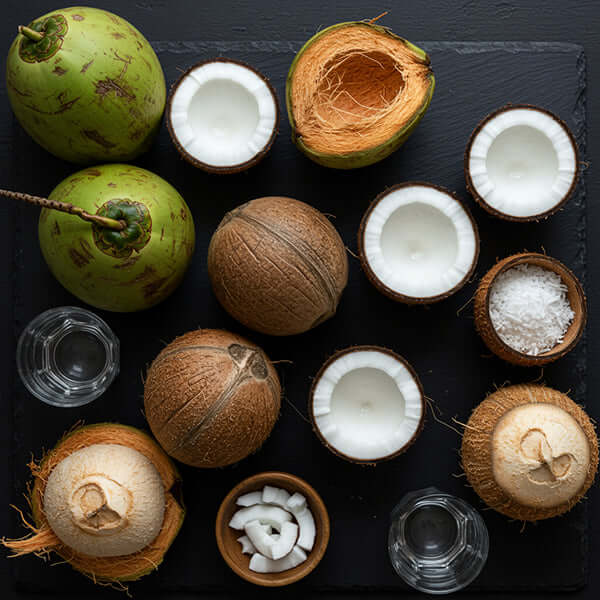 Various coconuts displayed on a slate board, showcasing their textures and contents including coconut water and coconut meat.