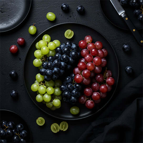 A variety of fresh grapes including green, black, and red grapes displayed on a black plate.
