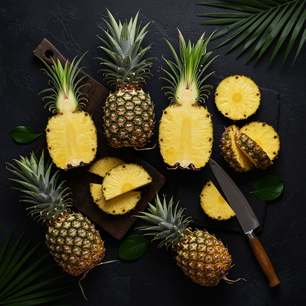 Fresh pineapples cut and whole, showcasing their juicy yellow insides and vibrant green leaves.