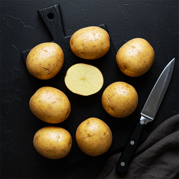 Fresh potatoes arranged on a cutting board, showcasing whole and halved Potato.